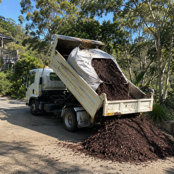 Tip truck unloading dark hardwood mulch onto a driveway.