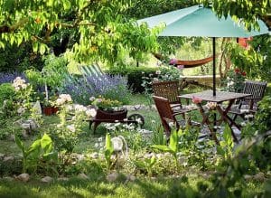Wooden table and chairs in a beautiful garden. Landscape design of country houses. Chairs and place under an umbrella in the garden under the trees in flower beds.